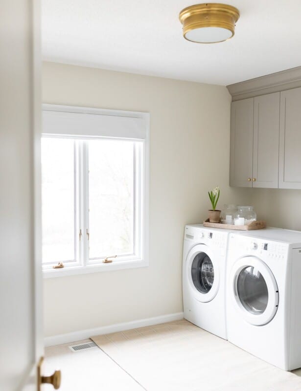 洗衣房，带有白色洗衣机和烘干机，金色灯具和白色墙壁和白色踢脚线