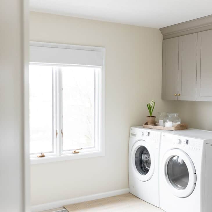 洗衣房有白色的洗衣机和烘干机，金色的灯具，白色的墙壁和白色的踢脚板