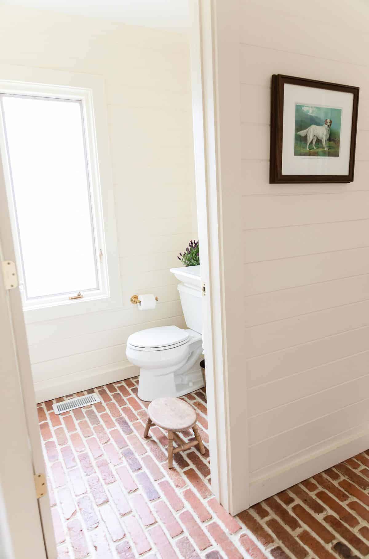 白色浴室，带有白色船盖，白色涂漆的踢脚线和砖地板，