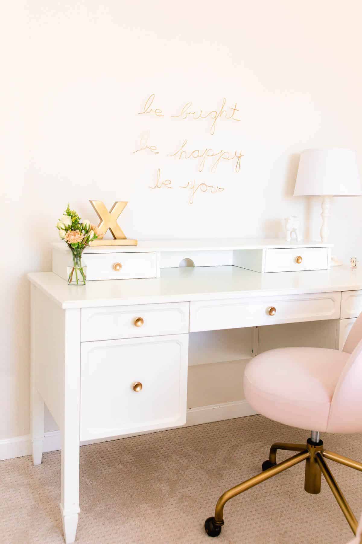 一个白色的桌子在女孩的卧室里，有白色的墙壁和粉红色的椅子。