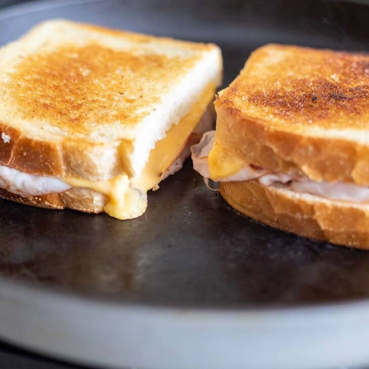 两个烤火腿和奶酪三明治放在黑色铸铁平底锅上。gydF4y2Ba