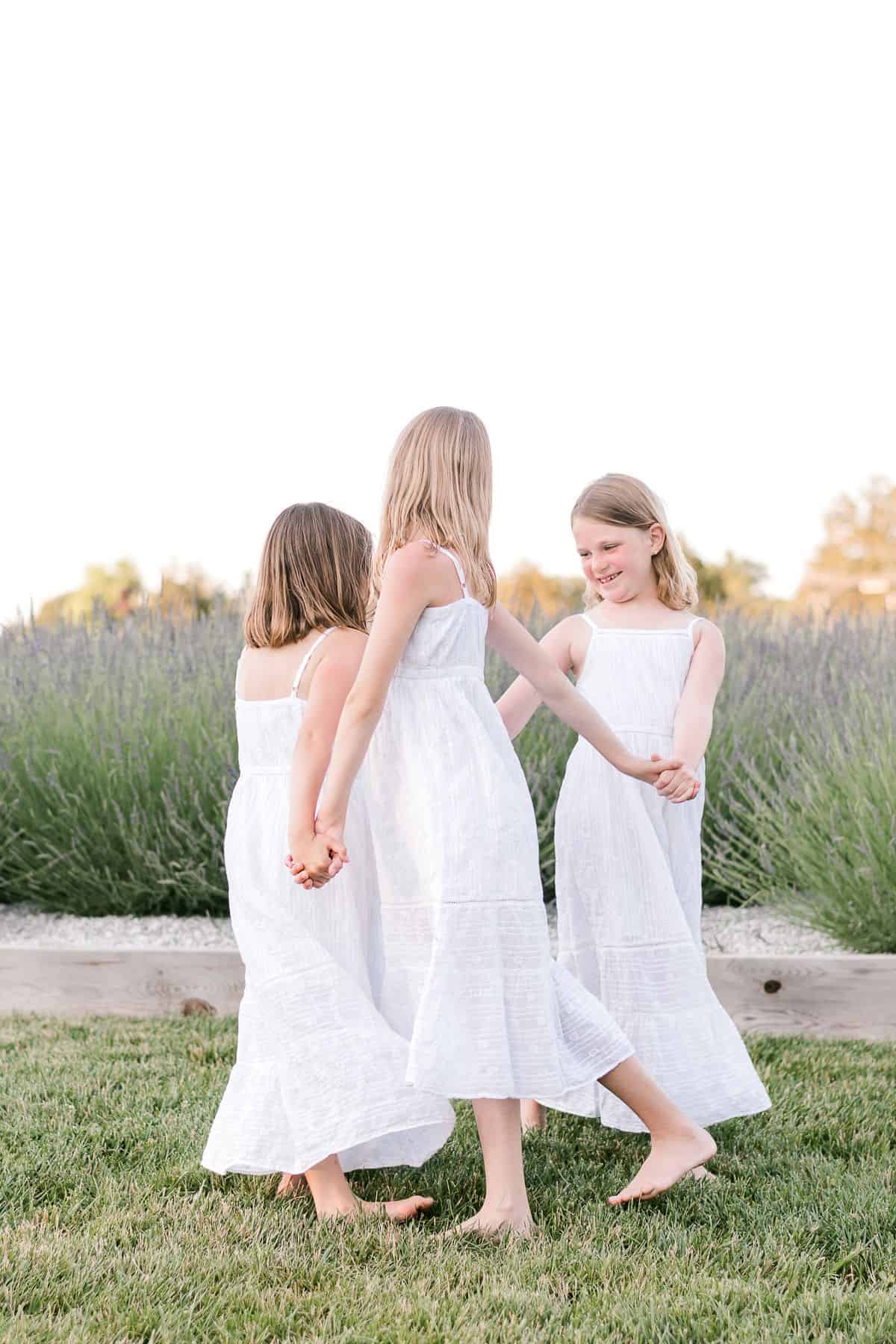 三个穿着白色连衣裙的小女孩在英国薰衣草的田野里跳舞。
