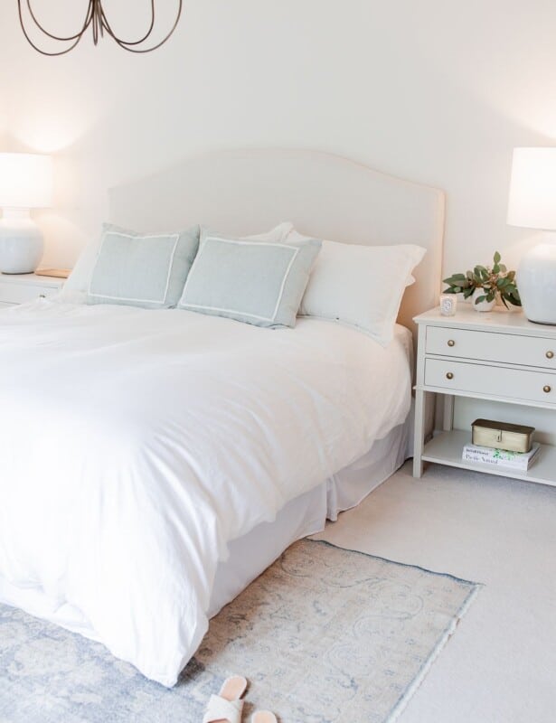 一间白色的卧室，床下有老式地毯的卧室地毯放置。