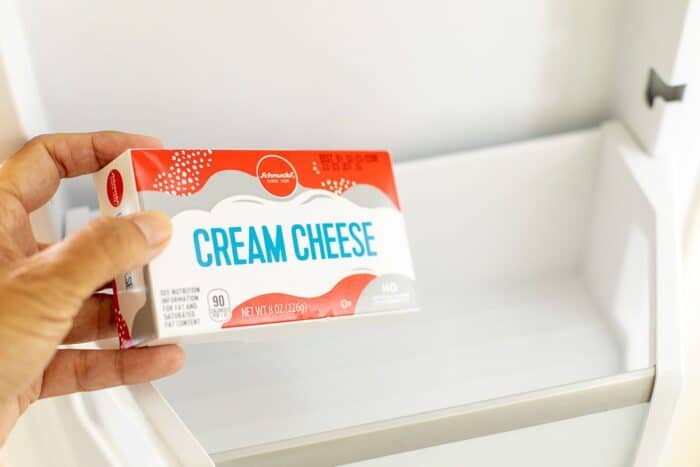 将一包奶油奶酪的手放在冰箱中。