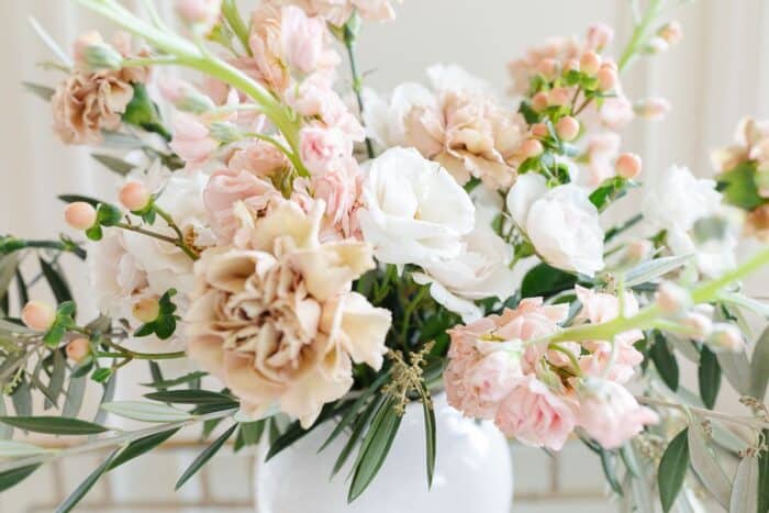 近距离古董康乃馨石竹和更多的花朵在色调的米色和奶油在一个白色的花瓶。
