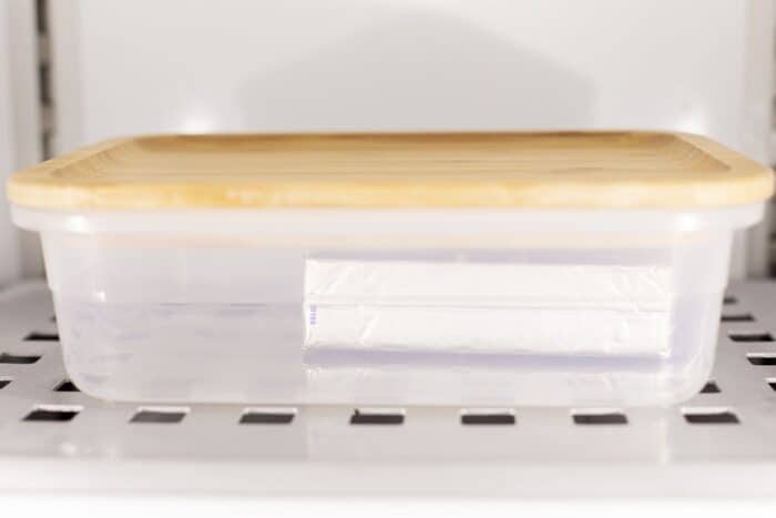 一块奶油奶酪，用箔纸包裹在塑料容器中，冰箱中的木制盖。