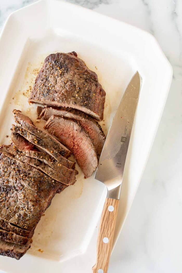 一个大型牛排，煮熟的中等稀有，切成白色拼盘上的切片，刀子到侧面。