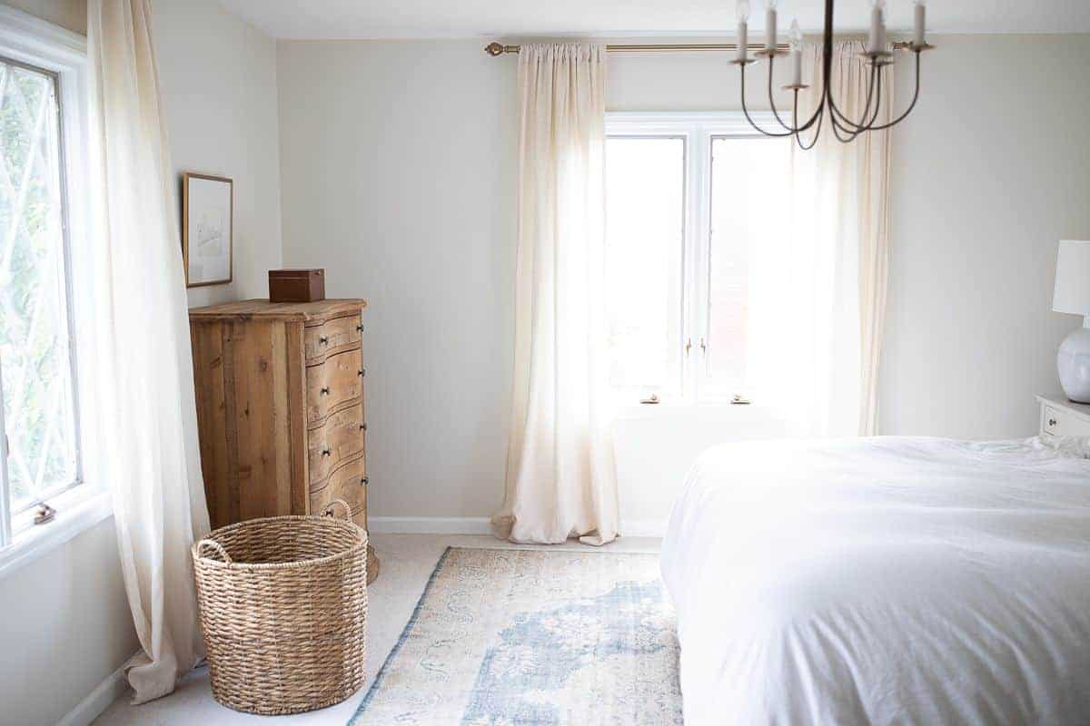 一个白色卧室，带木制梳妆台和床单的右尺寸地毯。