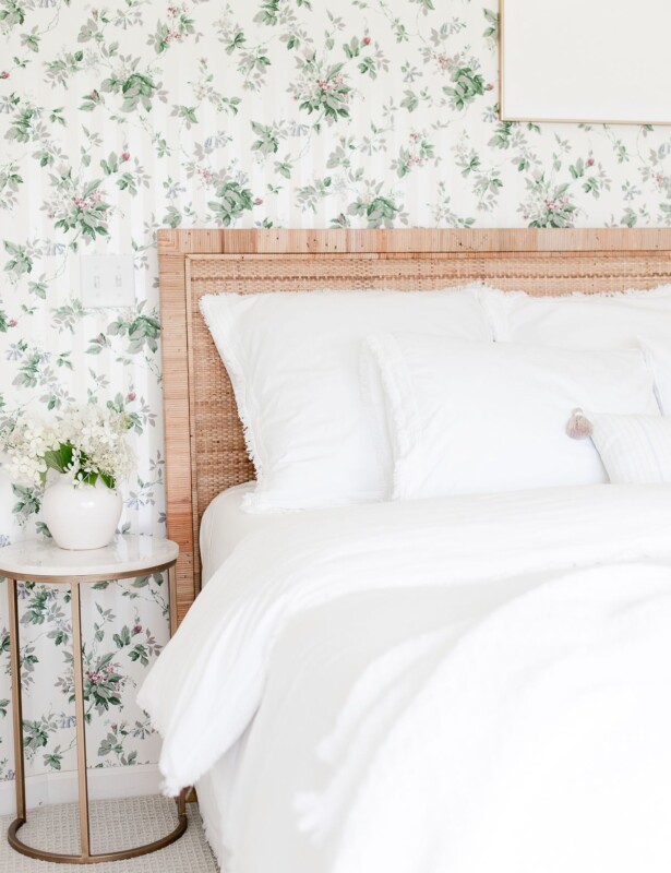 一间带花卉壁纸，藤垫，白色寝具和金色和大理石侧桌的卧室。