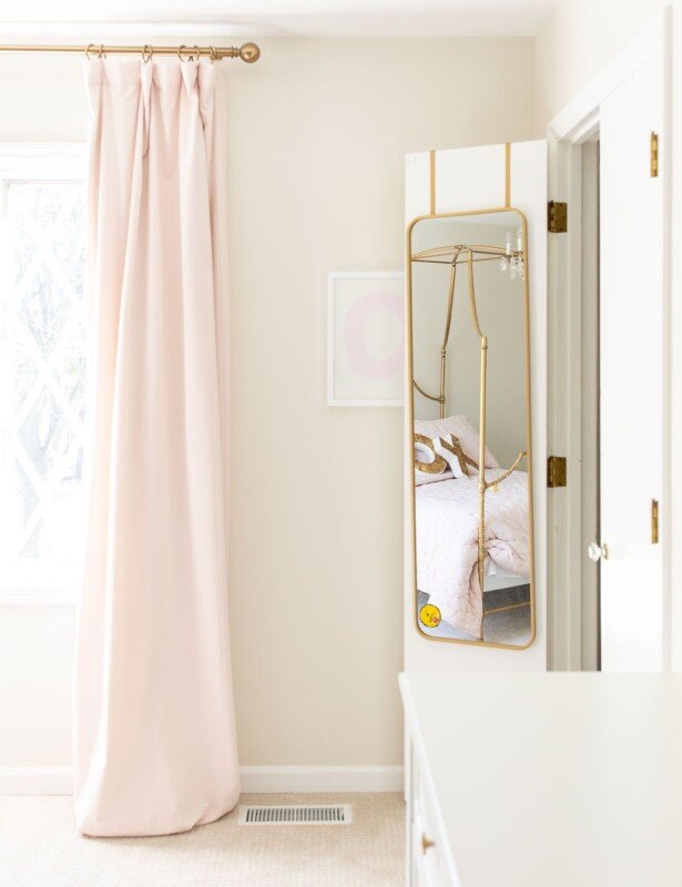 一个女孩的卧室，上面有粉红色的遮光窗帘和镜子挂在壁橱门上。