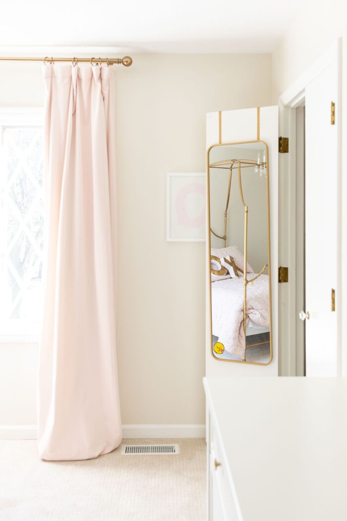 一个女孩的卧室，有粉红色的遮光窗帘，衣柜门上挂着一面镜子。