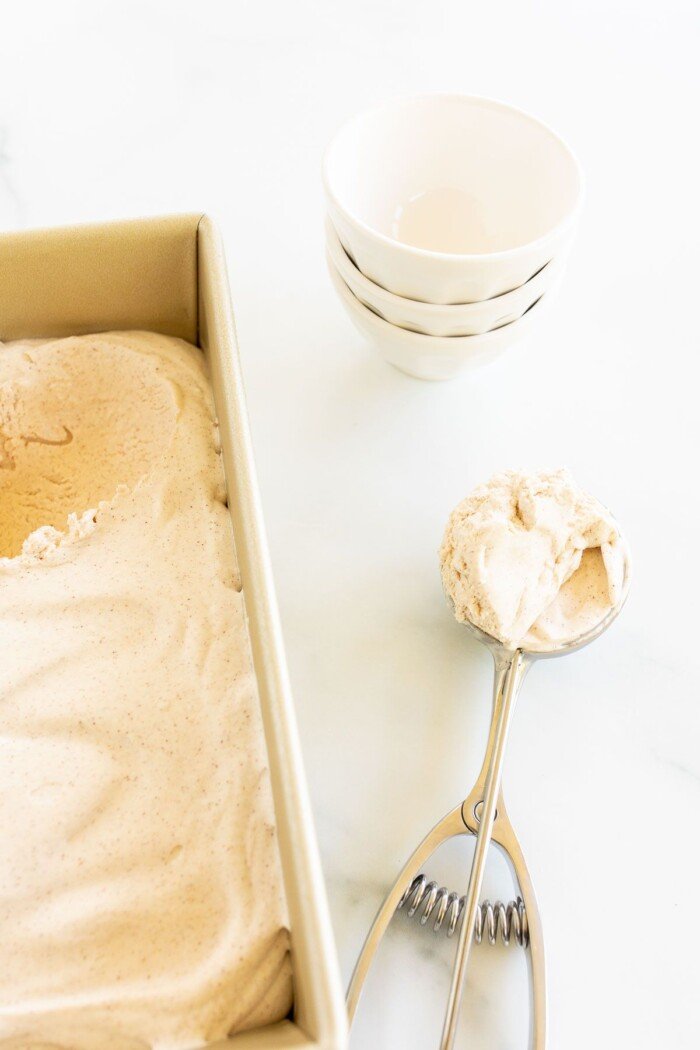 一个装满肉桂冰淇淋的金面包盘，侧面有一勺，背景碗GydF4y2Ba