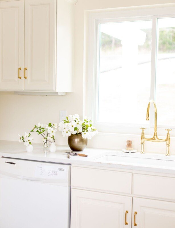 白色石英台面，台面上的台面边缘放宽，奶油厨房的水槽上的黄铜水龙头。
