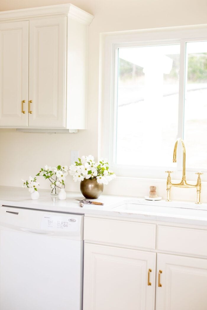 白色的石英台面带有缓和的台面边缘，奶油厨房的水槽上有黄铜水龙头。