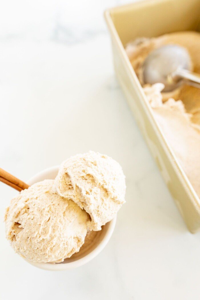 一个白碗，里面装满了自制肉桂冰淇淋，上面装饰着肉桂棒，侧面装饰，一个金面包锅，装满冰淇淋的背景GydF4y2Ba
