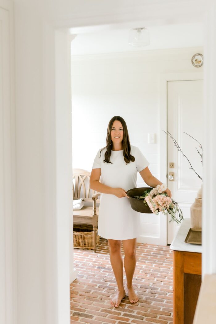 在一间白色的房间里，一个穿着白色连衣裙的女人，拿着一盒鲜花