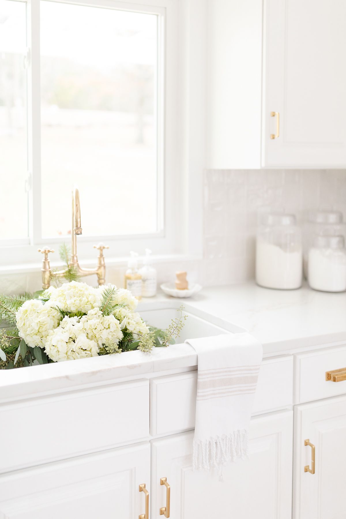 一个白色厨房，水槽中有花朵，黄铜龙头和白色后挡板