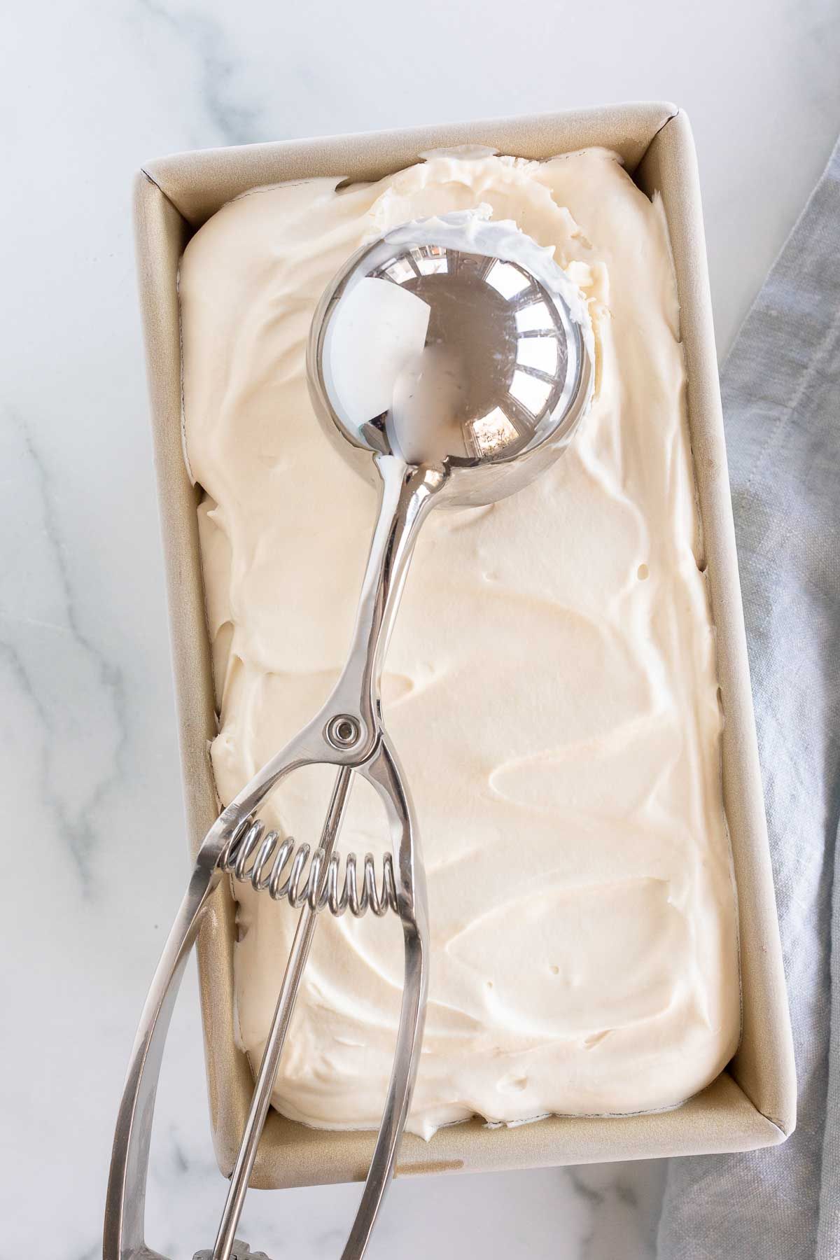 一个金色的面包盘装满自制的马斯卡彭冰淇淋，冰淇淋勺放在上面