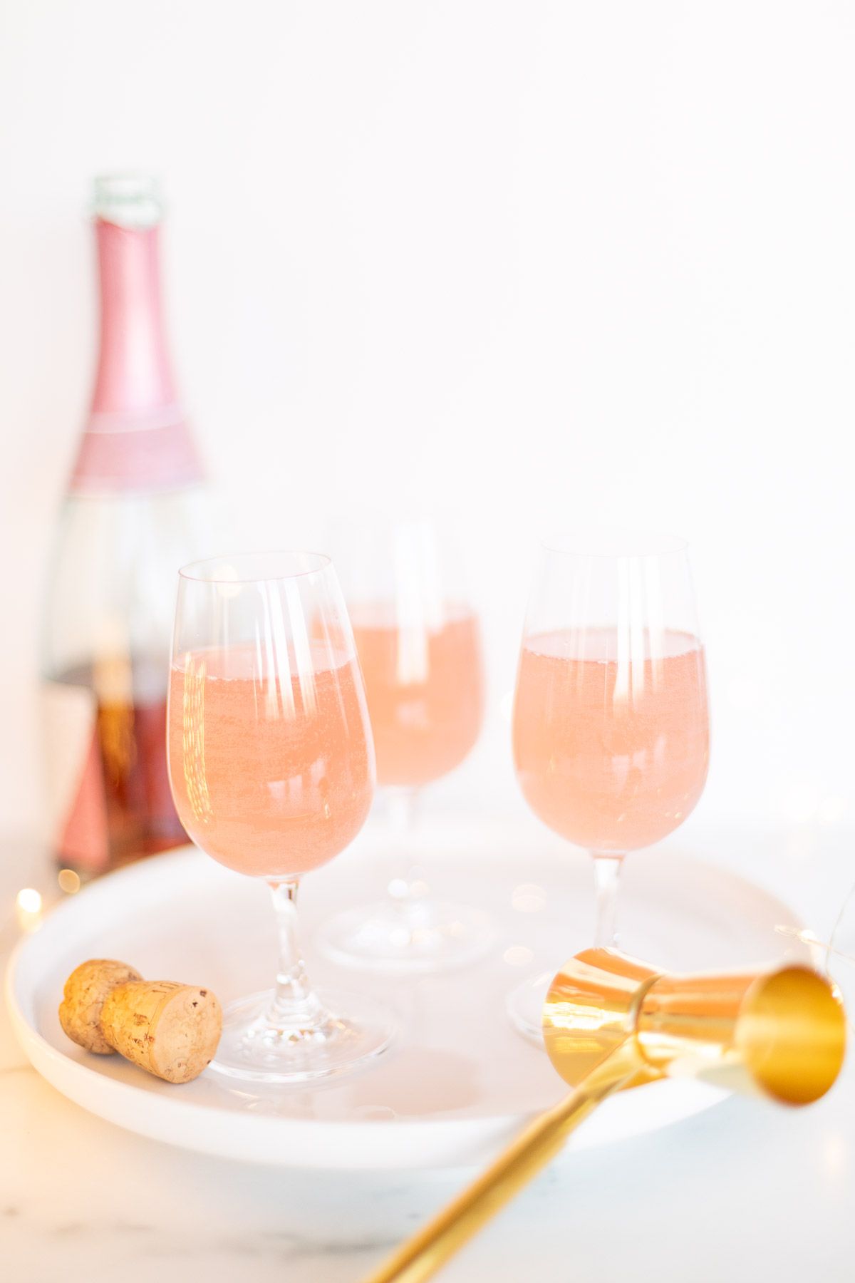 3杯香槟玛格丽塔酒在一个白色盘子，金五彩纸屑周围的金五彩纸屑和一个瓶桃红色香槟在背景中GydF4y2Ba