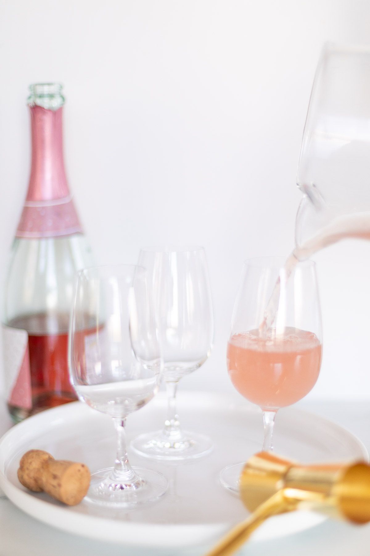 3个鸡尾酒杯在白色托盘上，用玻璃投手倒入粉红色的鸡尾酒。GydF4y2Ba