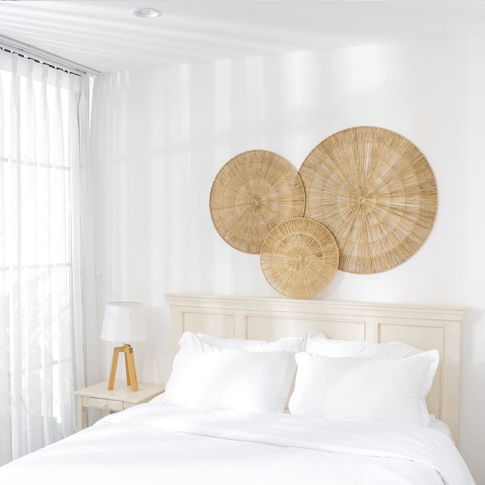 一间白色的卧室，床的上方挂着三个海草围成的圆圈作为艺术品