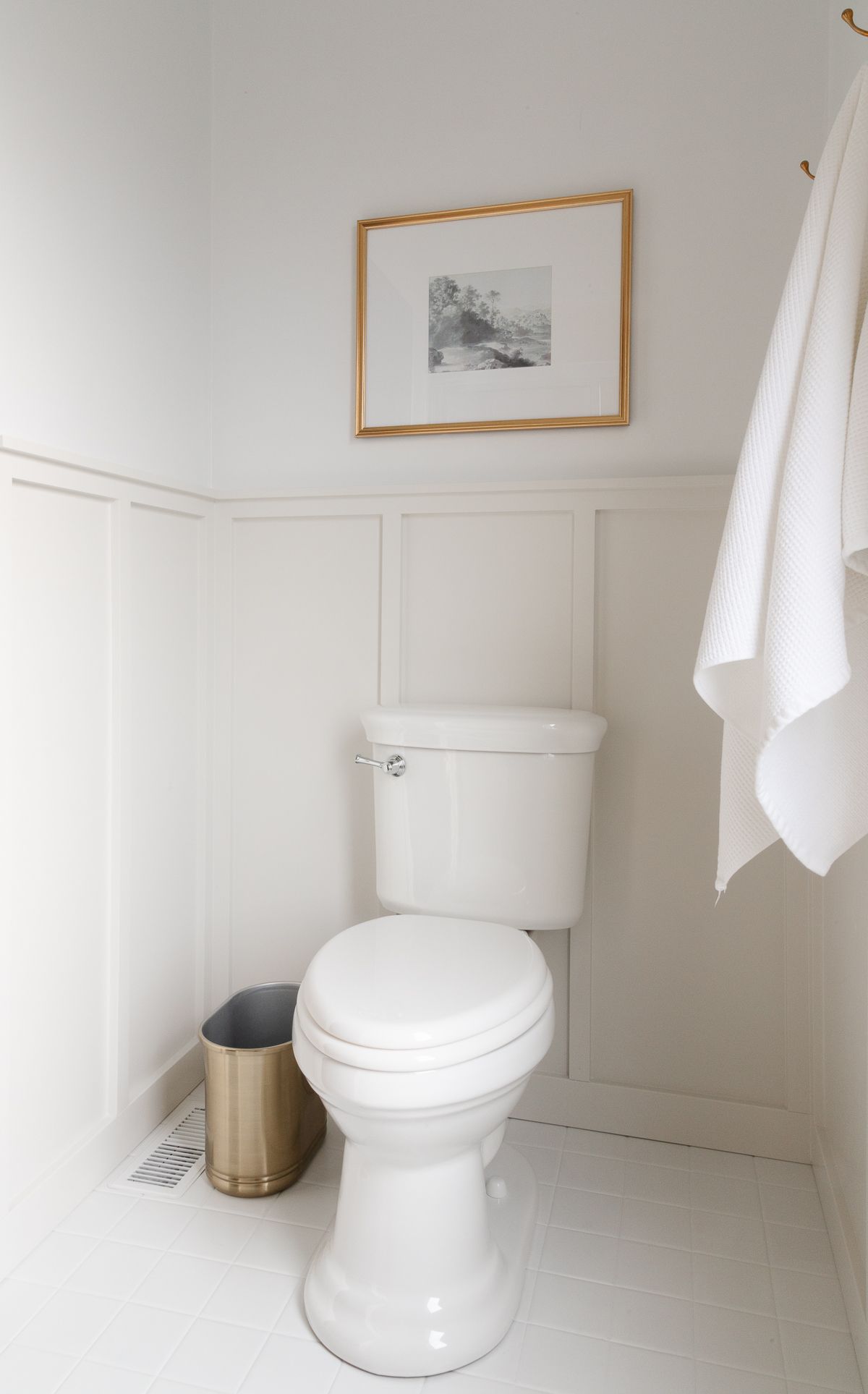 一间白色和灰色的浴室，空间周围有护壁板，上面是本杰明摩尔(Benjamin Moore)装饰公司的白色涂料。