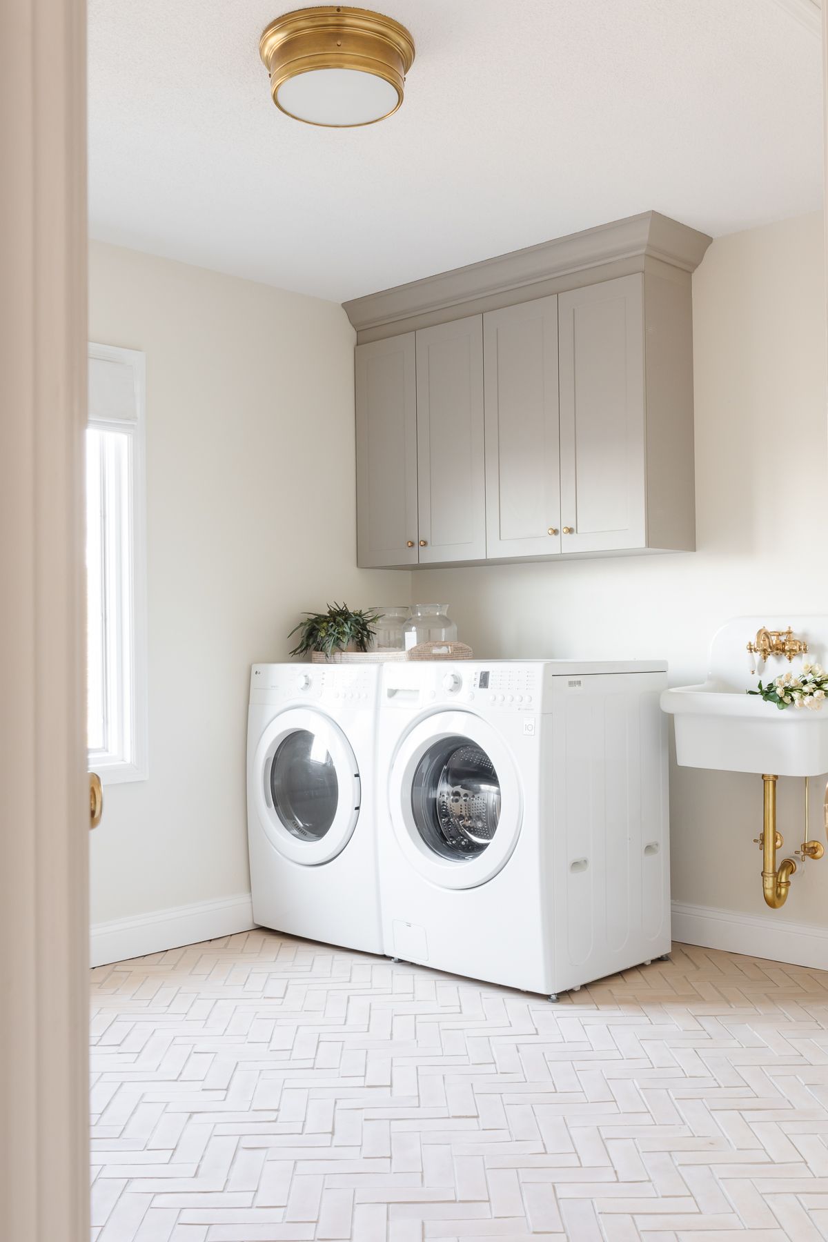 一间洗衣房，里面有灰色的橱柜、墙式洗涤槽和人字形地板。