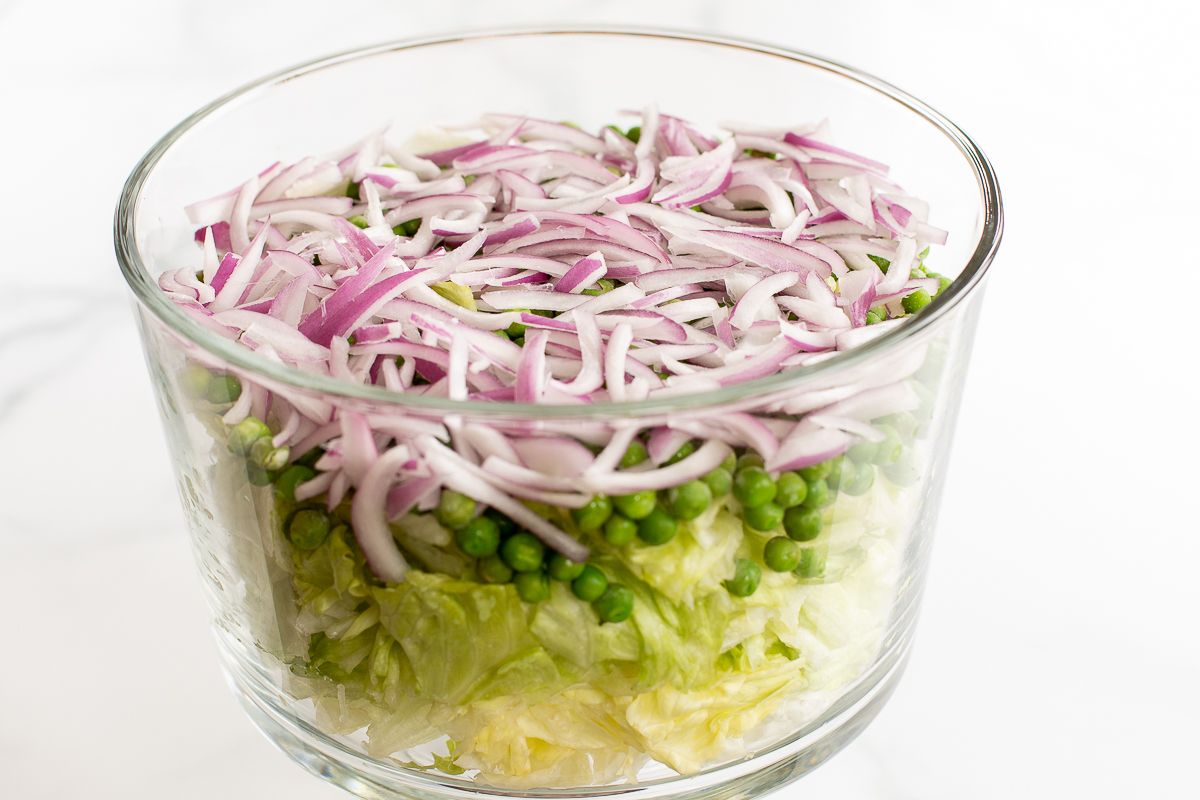 切碎的生菜，上面撒上豌豆和洋葱，放在玻璃盘子里。gydF4y2Ba
