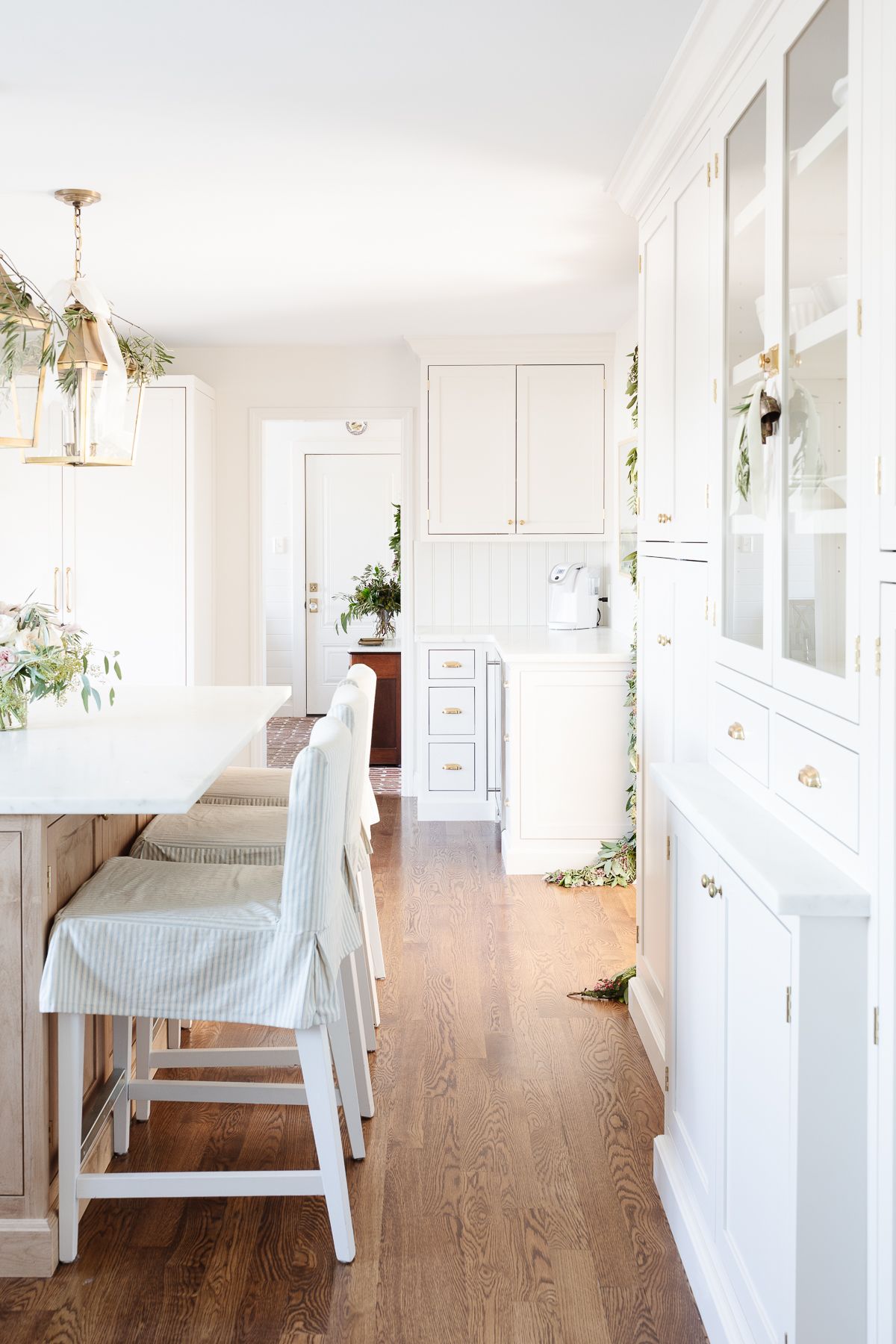 一间白色的厨房，有一个木制的岛台和一个镶板的冰箱，冰箱上有黄铜的电器拉杆