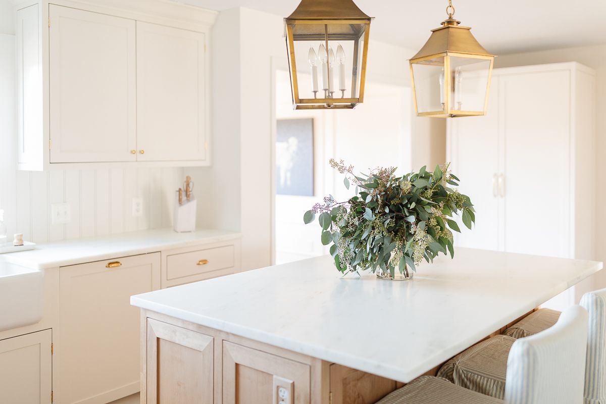 一间白色的厨房，有一个木制的岛台和一个镶板的冰箱，冰箱上有黄铜的电器拉杆