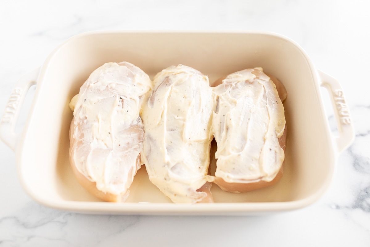 三个鸡胸肉覆盖在蛋黄酱的白色烤盘中。GydF4y2Ba