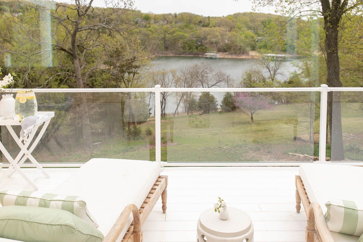 一个带有玻璃栏杆的白色甲板，有两把木制休息室椅和一间陶瓷花园中间。