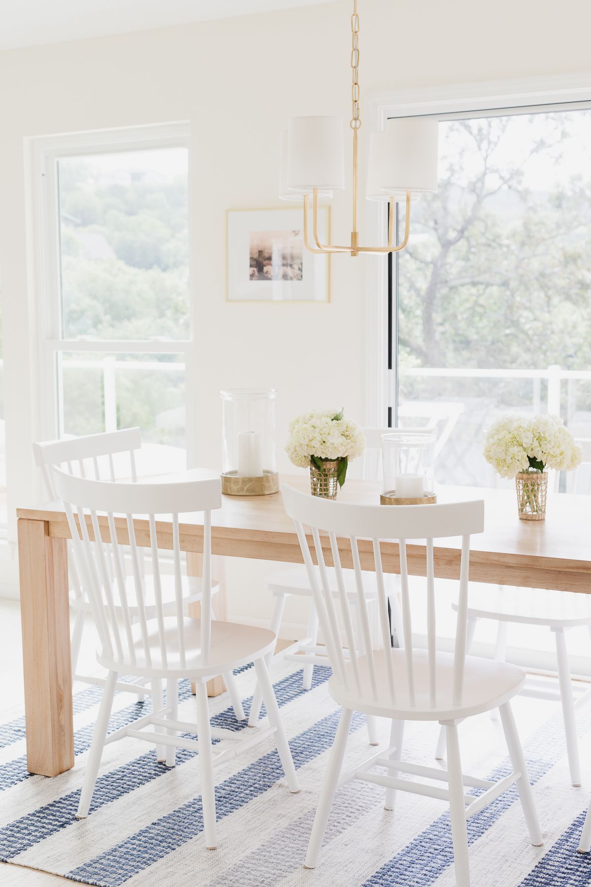 一张柚木餐桌，白色椅子放在蓝白条纹的地毯上