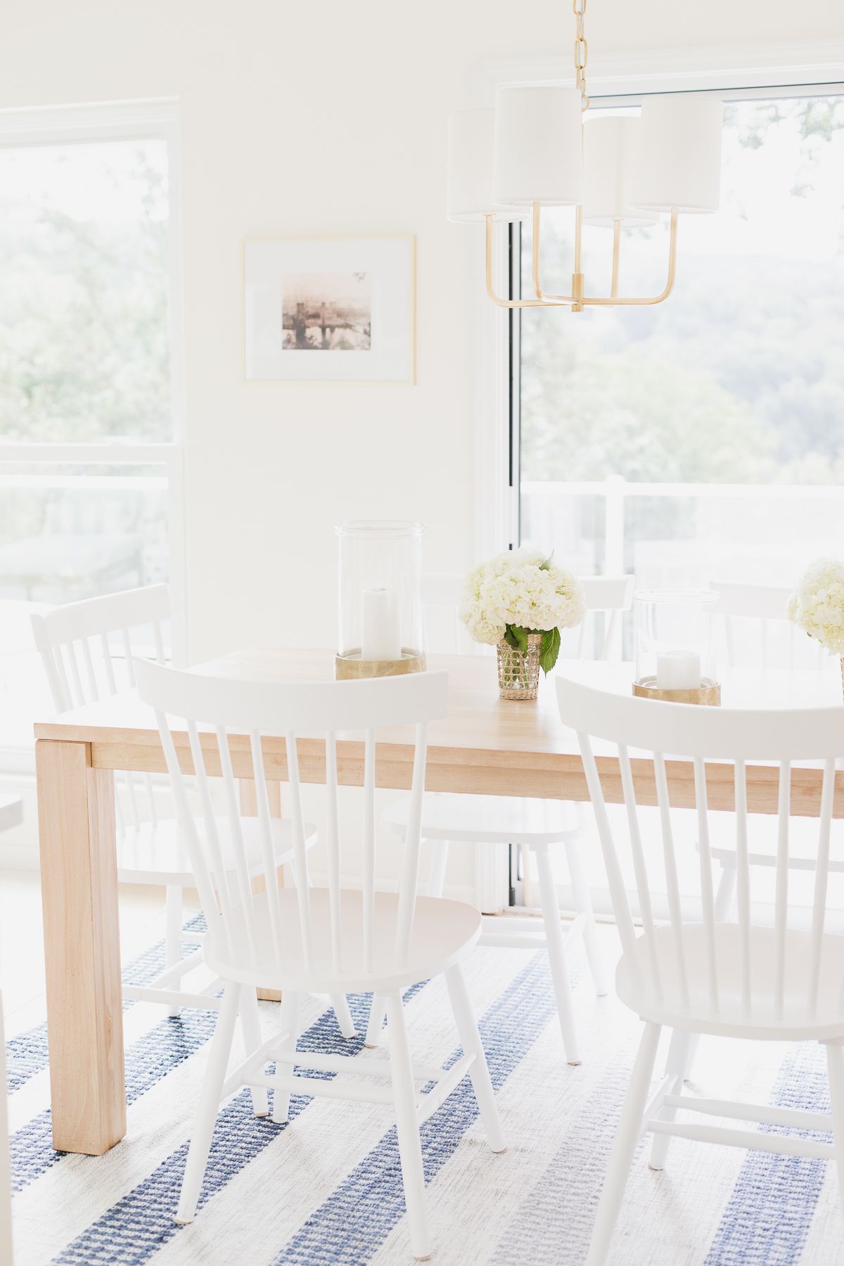 一张柚木餐桌，白色椅子放在蓝白条纹的地毯上
