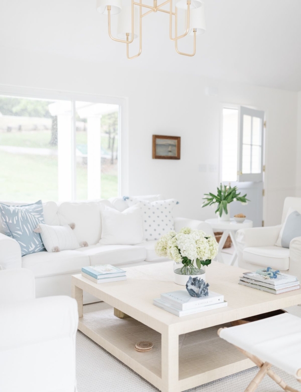 一个明亮的白色客厅，带有白色套餐的沙发和浅蓝色枕头