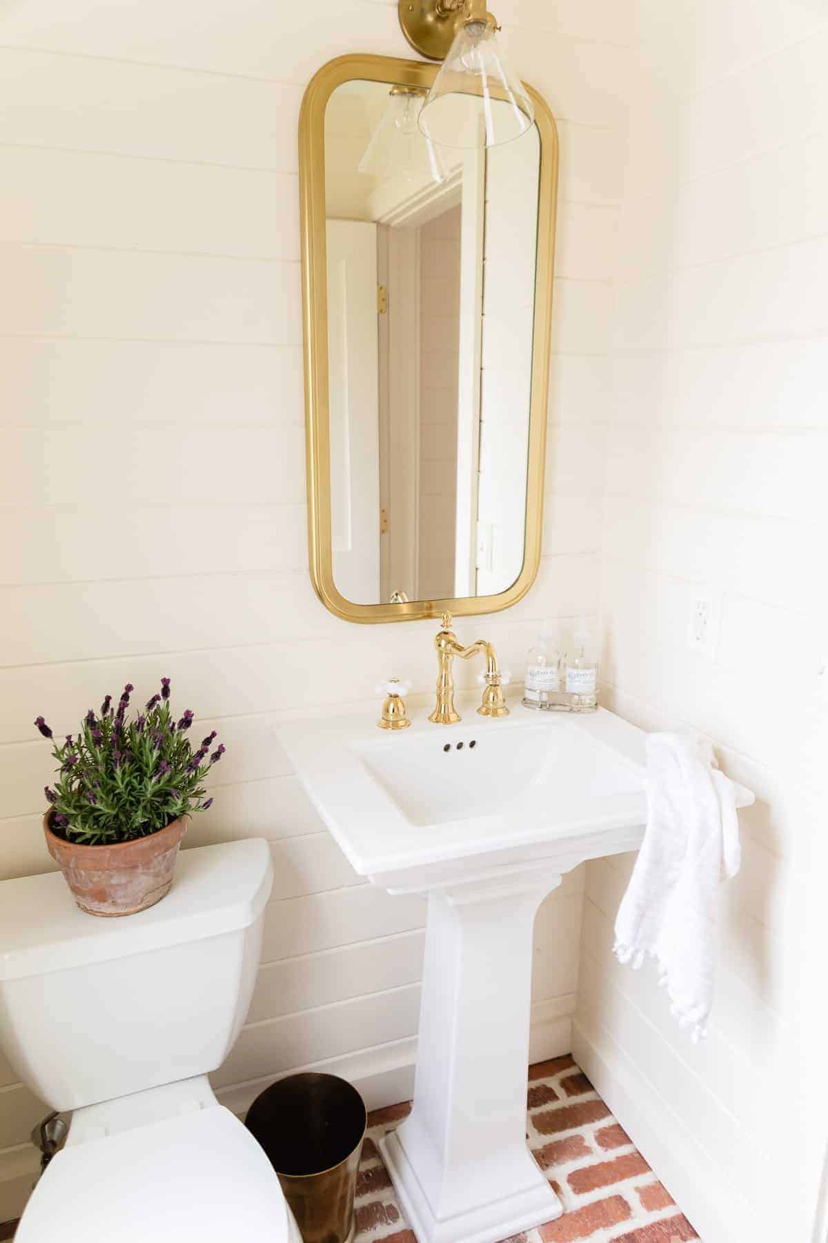 浴室里镜子和洗手池上方的黄铜壁龛，马桶上放着一盆法国薰衣草