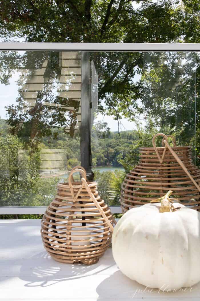 白色的露台上有玻璃栏杆，两盏藤条灯笼和一个白色南瓜，是极简主义的秋季装饰。