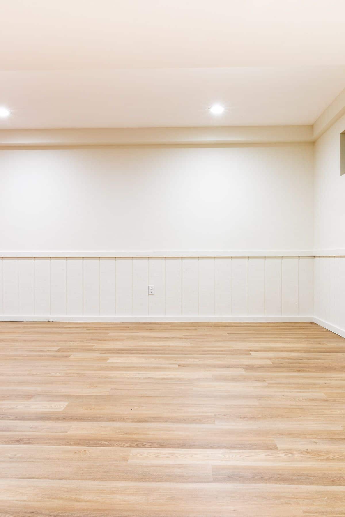 一个空的地下室，白色的墙壁和中等色调的乙烯基板材地板。