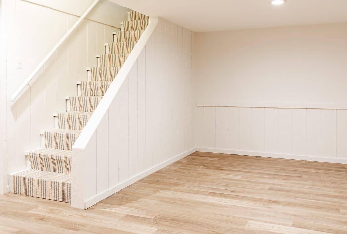 一个空的地下室，白色的墙壁和中等色调的乙烯基板材地板。