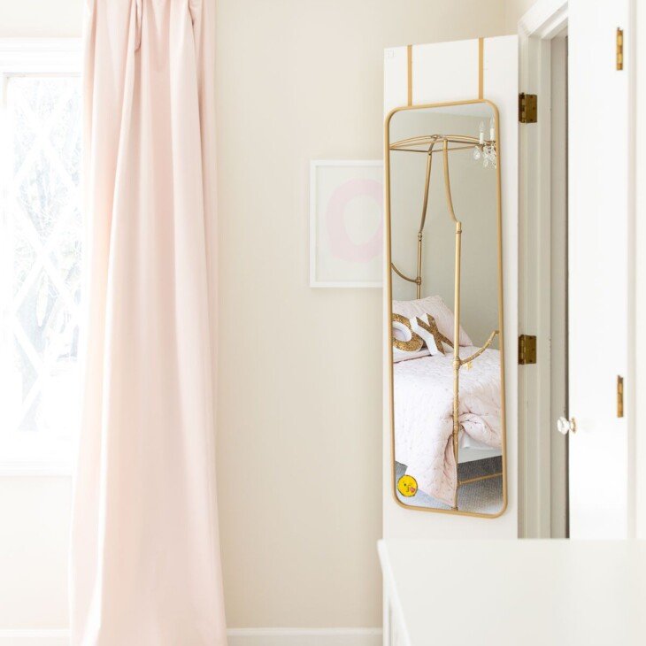 一个女孩的卧室，上面有粉红色的遮光窗帘和镜子挂在壁橱门上。